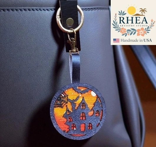 Rhea Artistry Studio Halloween haunted house charm with spiderweb on vegetable-tanned leather, attached to a black bag.