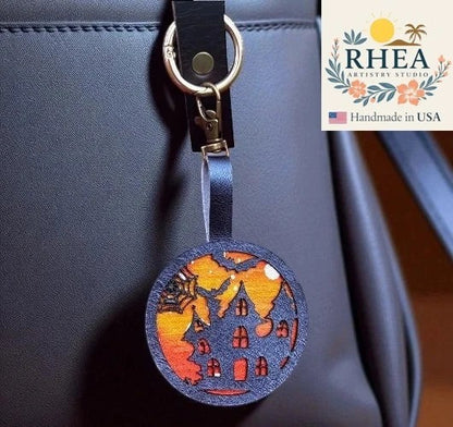 Rhea Artistry Studio Halloween haunted house charm with spiderweb on vegetable-tanned leather, attached to a black bag.