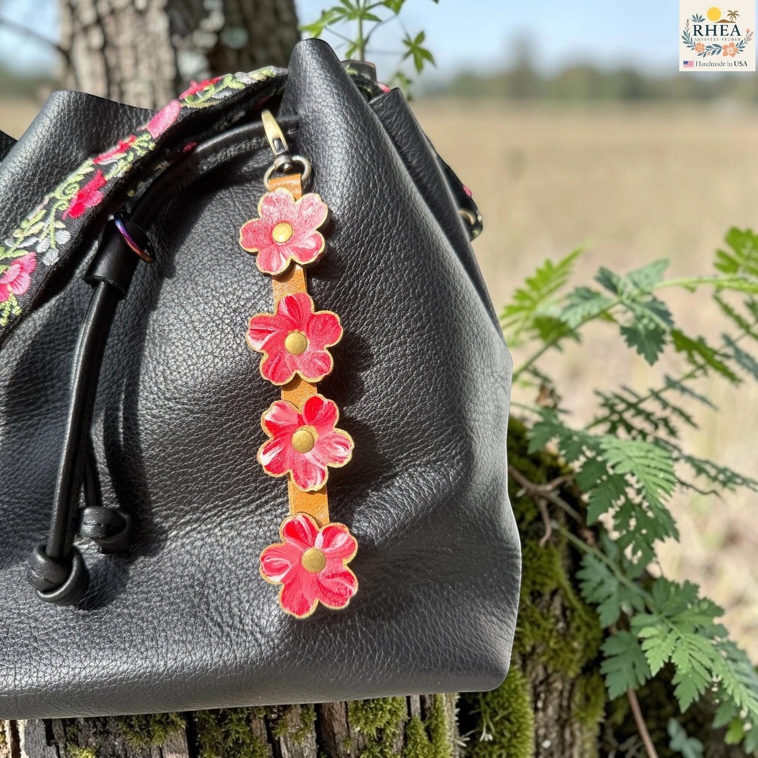 Rhea Artistry Studio Hand-Painted Leather Flower Bag Charm in Cherry Blush with red, pink, and white painted leather flowers, brass rivets, honey leather strap, and antique brass clasp.