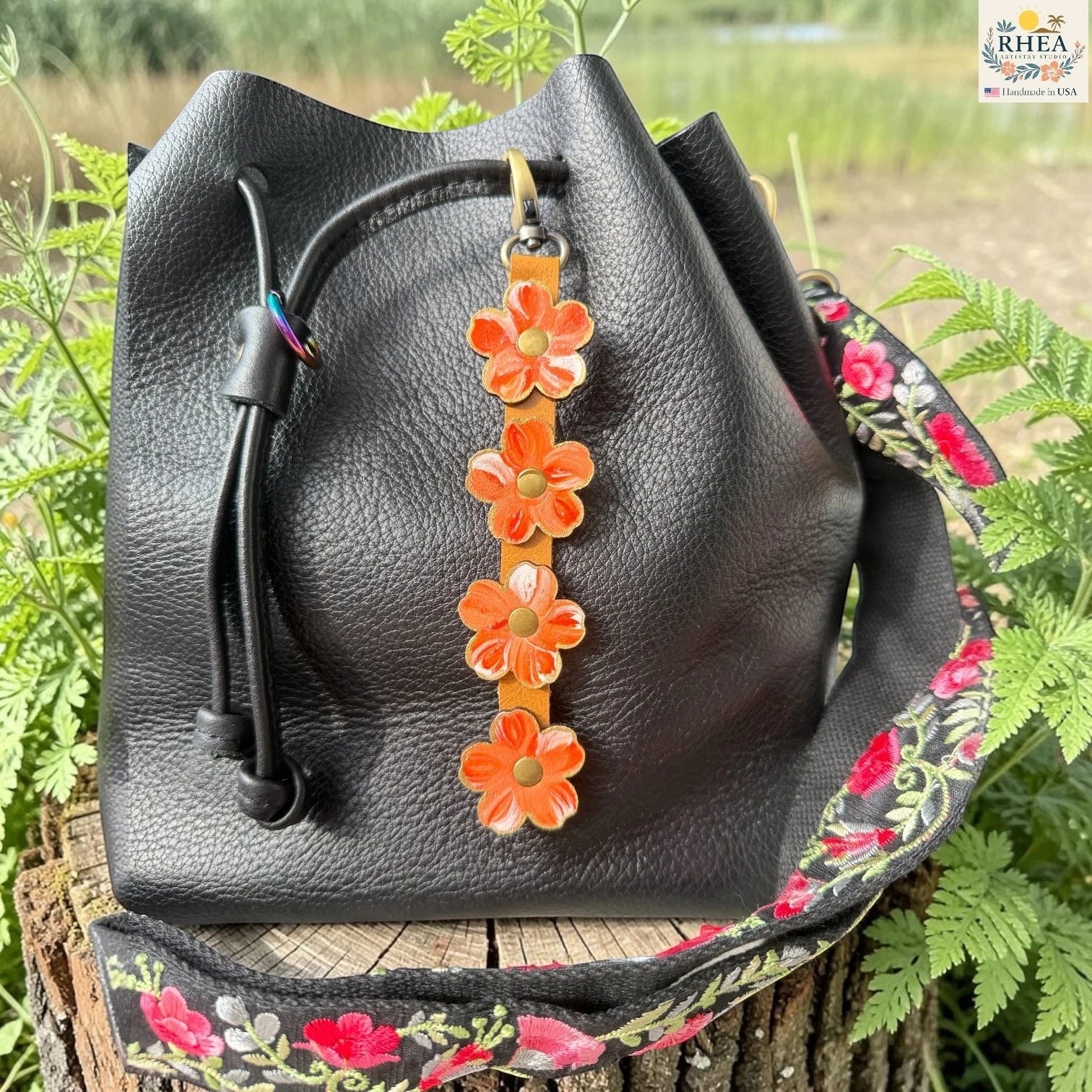 Rhea Artistry Studio Hand-Painted Leather Flower Bag Charm in Coral Honey with coral, orange, peach, and white painted leather flowers, brass rivets, honey leather strap, and antique brass clasp.