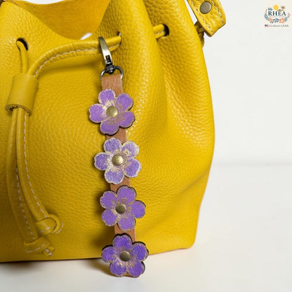 Rhea Artistry Studio Hand-Painted Leather Flower Bag Charm with lavender organic flower details, brass rivet centers, and antique brass hardware.