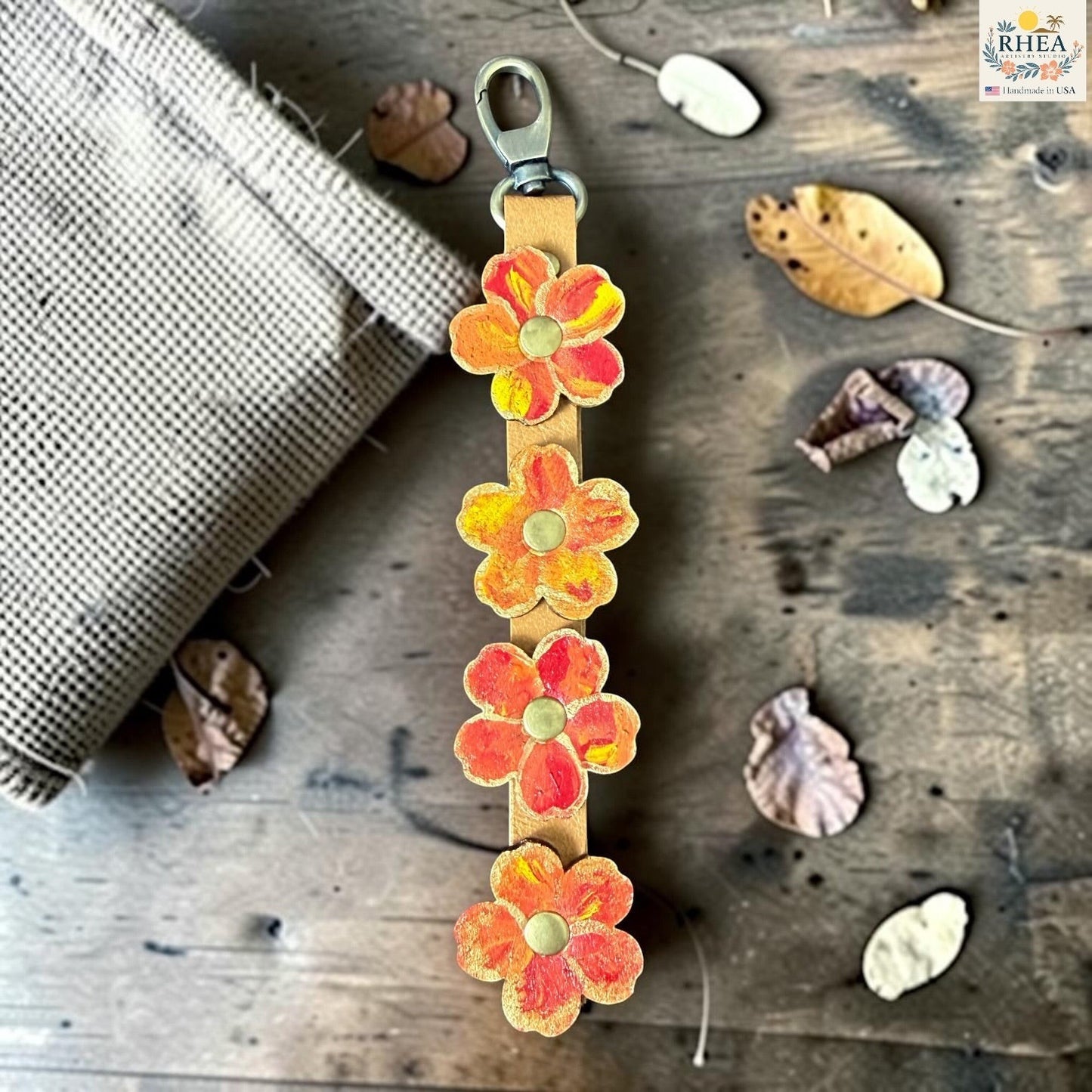 Rhea Artistry Studio Hand-Painted Leather Flower Bag Charm with orange, coral, and yellow organic flower details, brass rivet centers, and antique brass hardware.