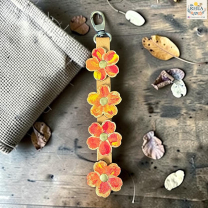 Rhea Artistry Studio Hand-Painted Leather Flower Bag Charm with orange, coral, and yellow organic flower details, brass rivet centers, and antique brass hardware.