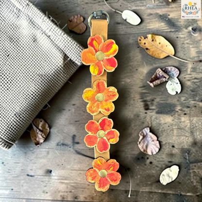 Rhea Artistry Studio Hand-Painted Leather Flower Bag Charm in Marigold Glow with orange and coral painted leather flowers, brass rivets, and antique brass clasp.