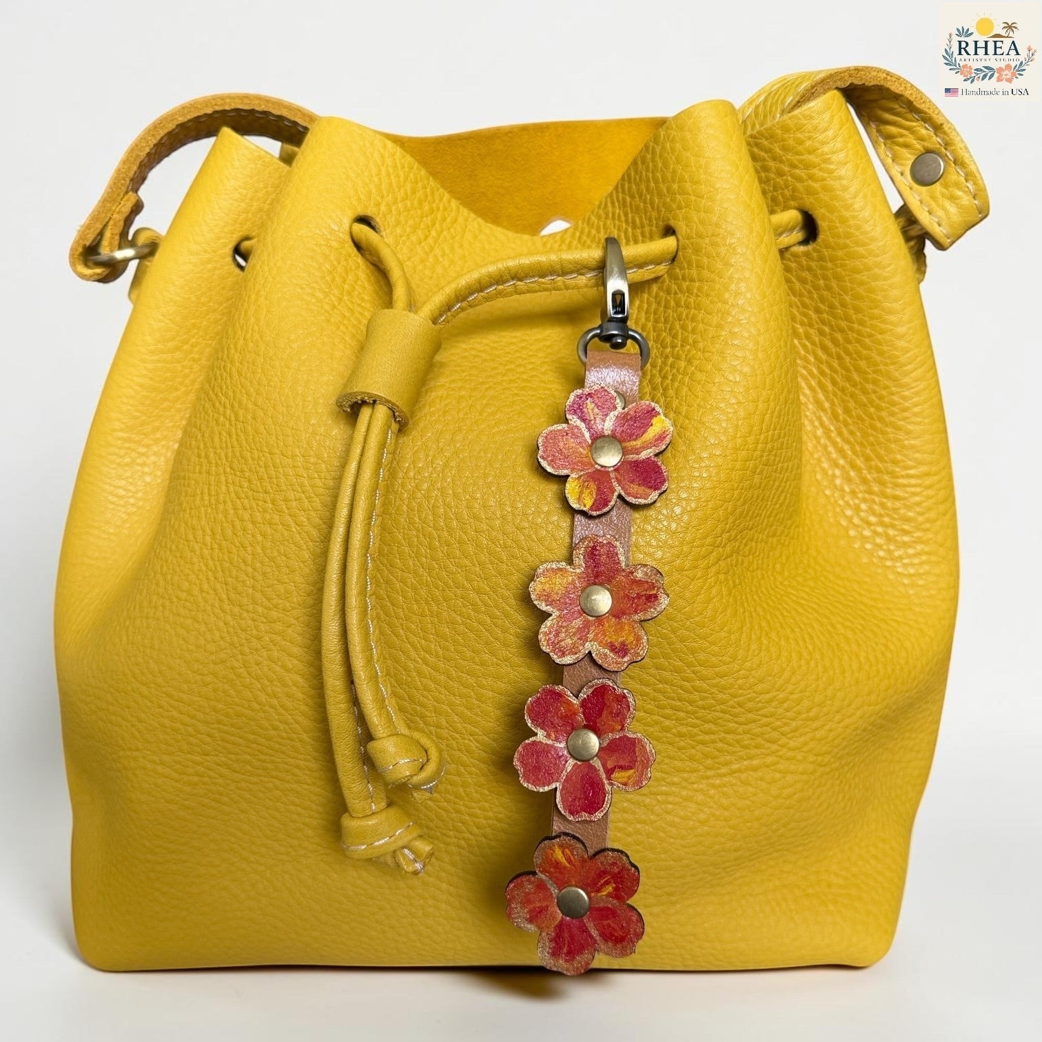 Rhea Artistry Studio Hand-Painted Leather Flower Bag Charm in Marigold Glow with sealed painted floral leather charms, brass rivets, and honey leather strap.