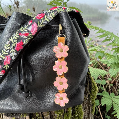 Rhea Artistry Studio Hand-Painted Leather Flower Bag Charm in Petal Cream with soft pale pink and cream painted leather flowers, brass rivets, honey leather strap, and antique brass clasp.