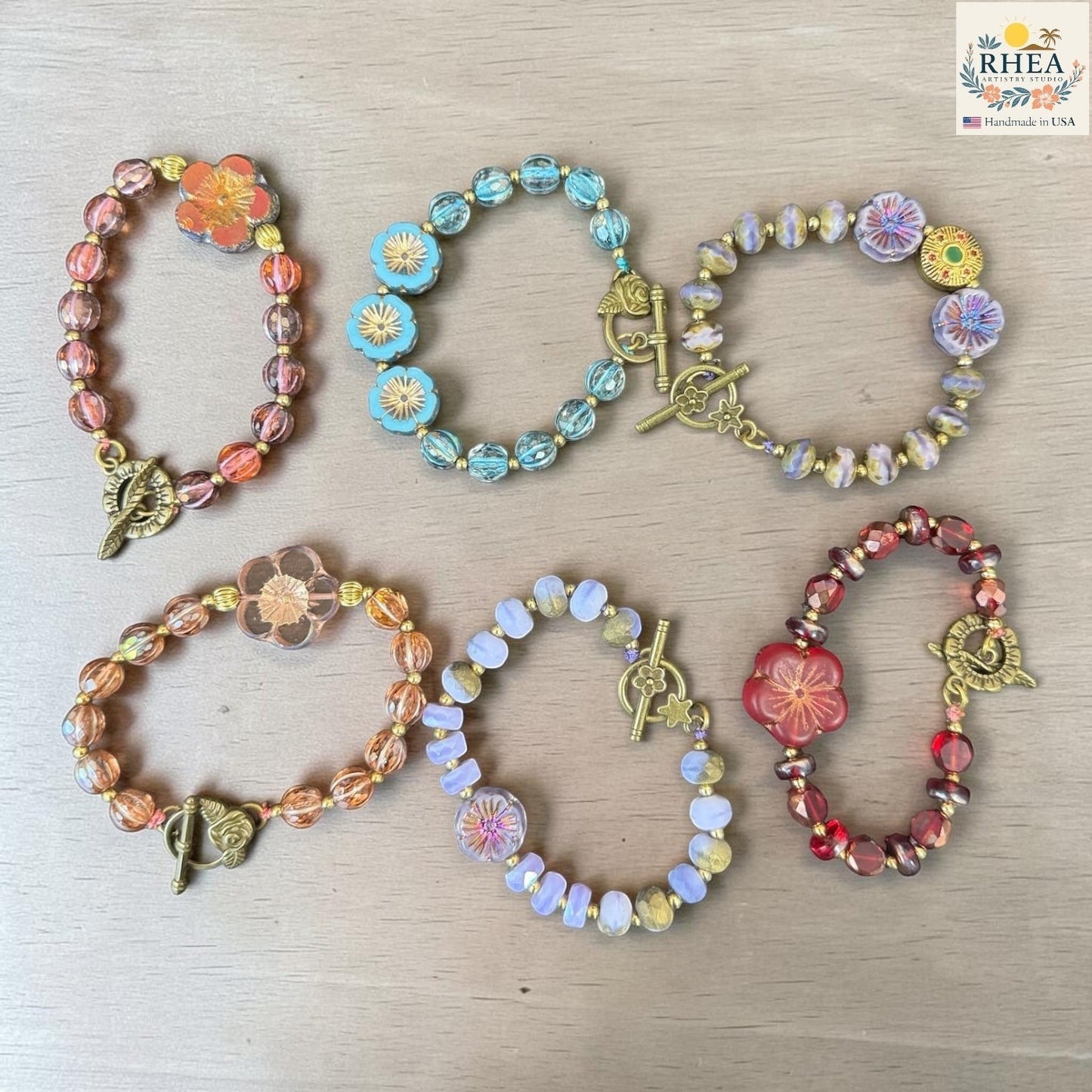 Rhea Artistry Studio handmade glass bead bracelets with floral focal beads in warm tones, blue, and red, featuring brass toggle clasps.