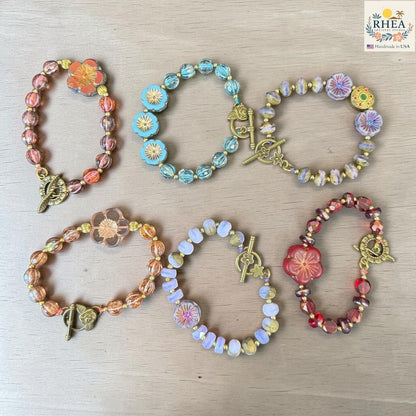 Rhea Artistry Studio handmade glass bead bracelets with floral focal beads in warm tones, blue, and red, featuring brass toggle clasps.