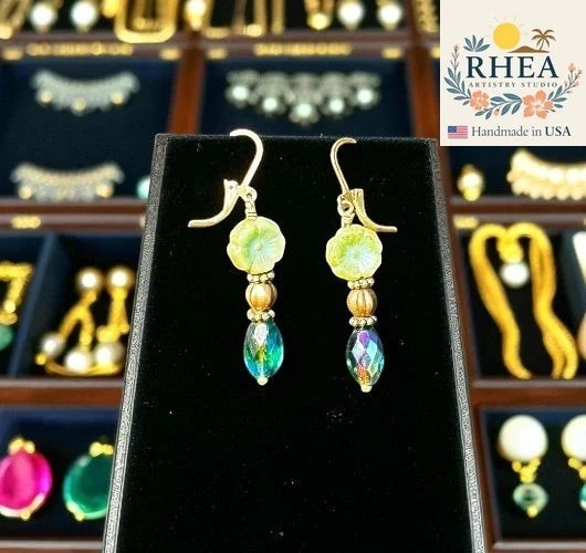 Rhea Artistry Studio light green glass hibiscus earrings with iridescent oval drop beads and gold accents. Approx. 1.5-2 inches long.