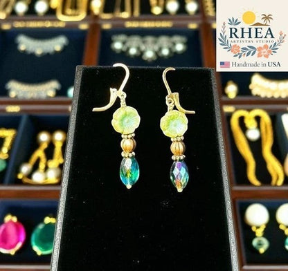 Rhea Artistry Studio light green glass hibiscus earrings with iridescent oval drop beads and gold accents. Approx. 1.5-2 inches long.