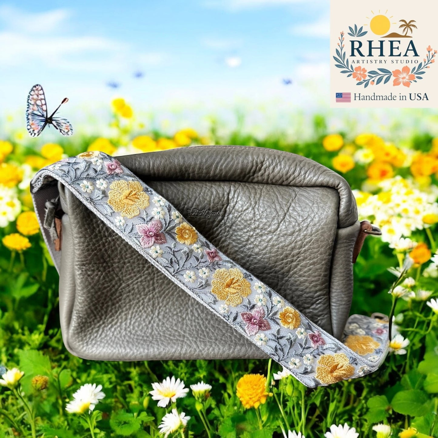 Rhea Artistry Studio grey crossbody bag with a 2-inch wide adjustable strap featuring embroidered yellow and pink hibiscus flowers on a light grey background.