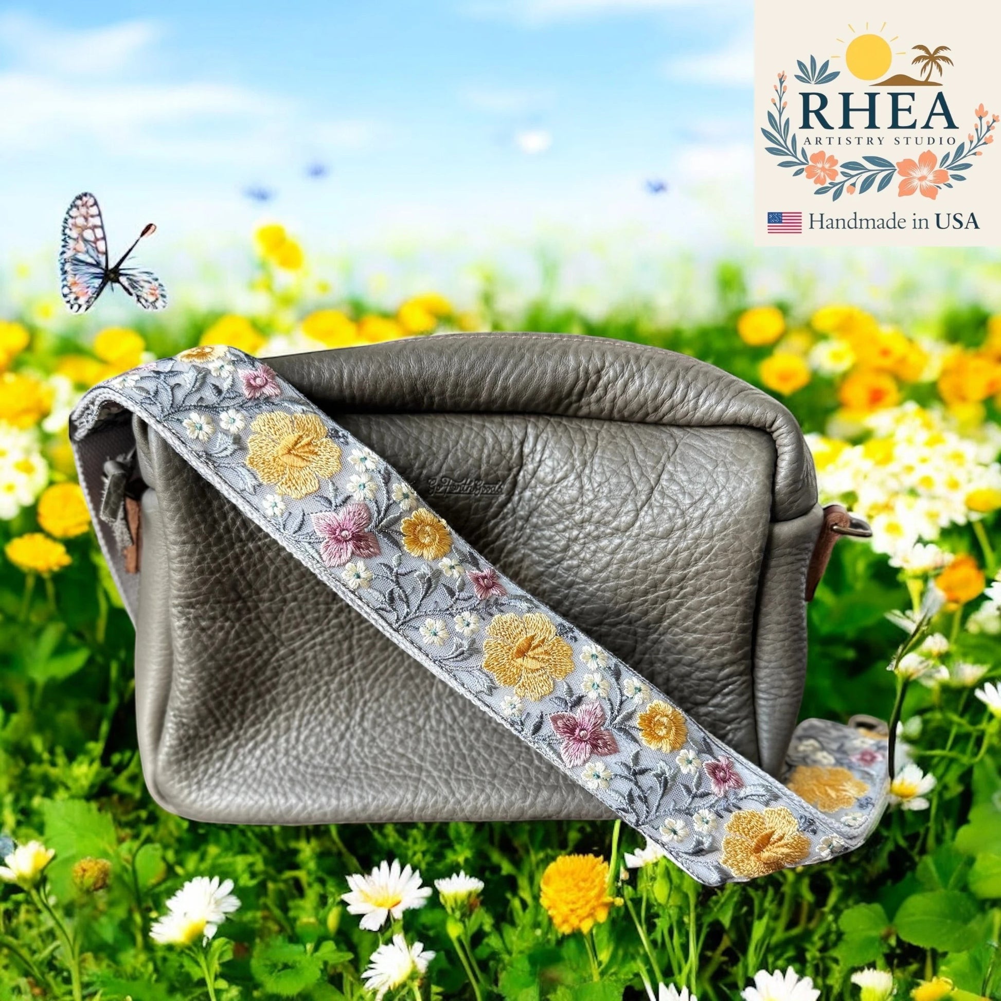 Rhea Artistry Studio grey crossbody bag with a 2-inch wide adjustable strap featuring embroidered yellow and pink hibiscus flowers on a light grey background.