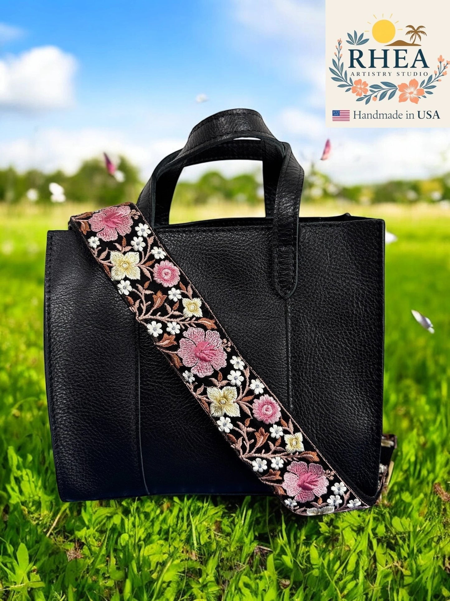 Rhea Artistry Studio black crossbody strap with pink and white hibiscus embroidery, 2-inch wide, adjustable length, brushed brass hardware.