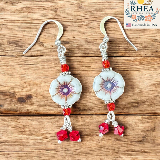 Rhea Artistry Studio white hibiscus glass floral earrings with red crystal accents and silver-plated hooks.