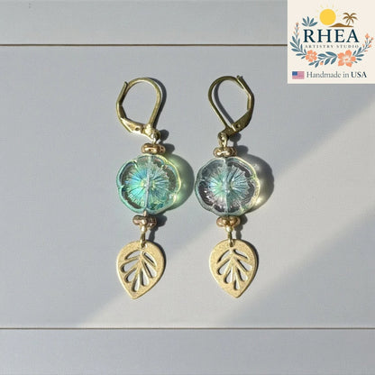 Rhea Artistry Studio handmade hibiscus glass drop earrings with gold leaf charms in iridescent blue-green.