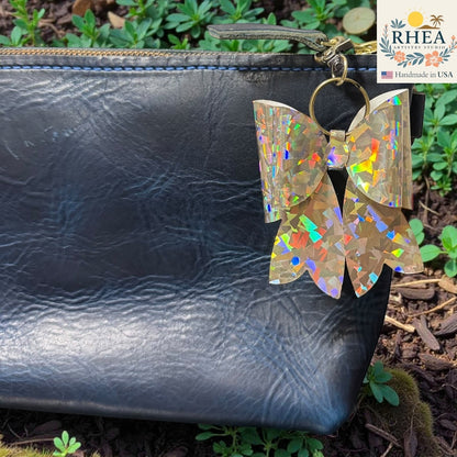 Rhea Artistry Studio holographic bow bag charm with brass hardware, handmade in USA.