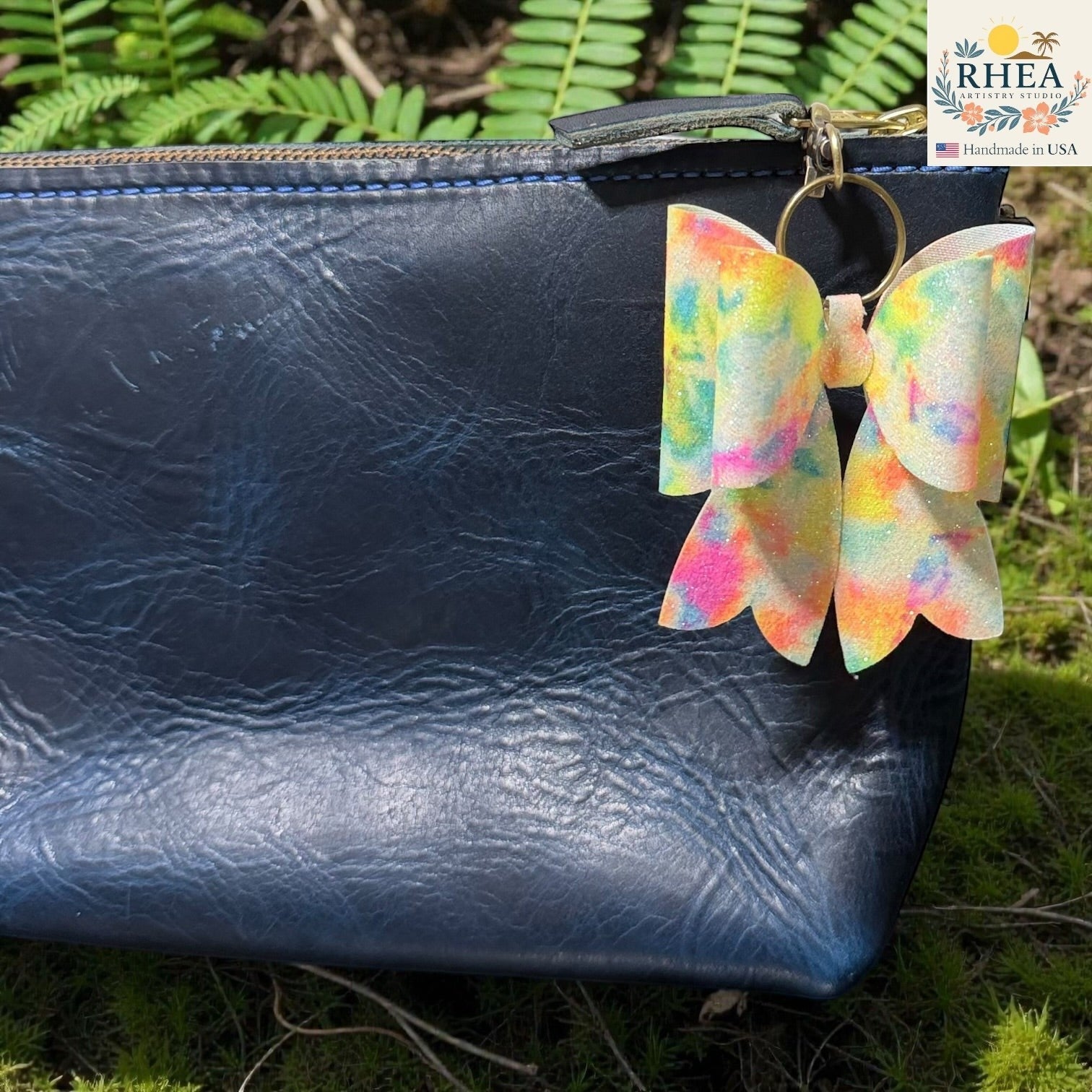 Rhea Artistry Studio handmade double-layer French bow bag charm with holographic tie-dye finish and brass hardware.
