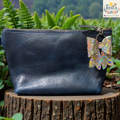 Rhea Artistry Studio holographic double-layer French bow bag charm with brass hardware, attached to a dark blue leather pouch.