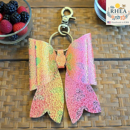 Rhea Artistry Studio handmade holographic pink and orange double-layer French bow bag charm with brass hardware.
