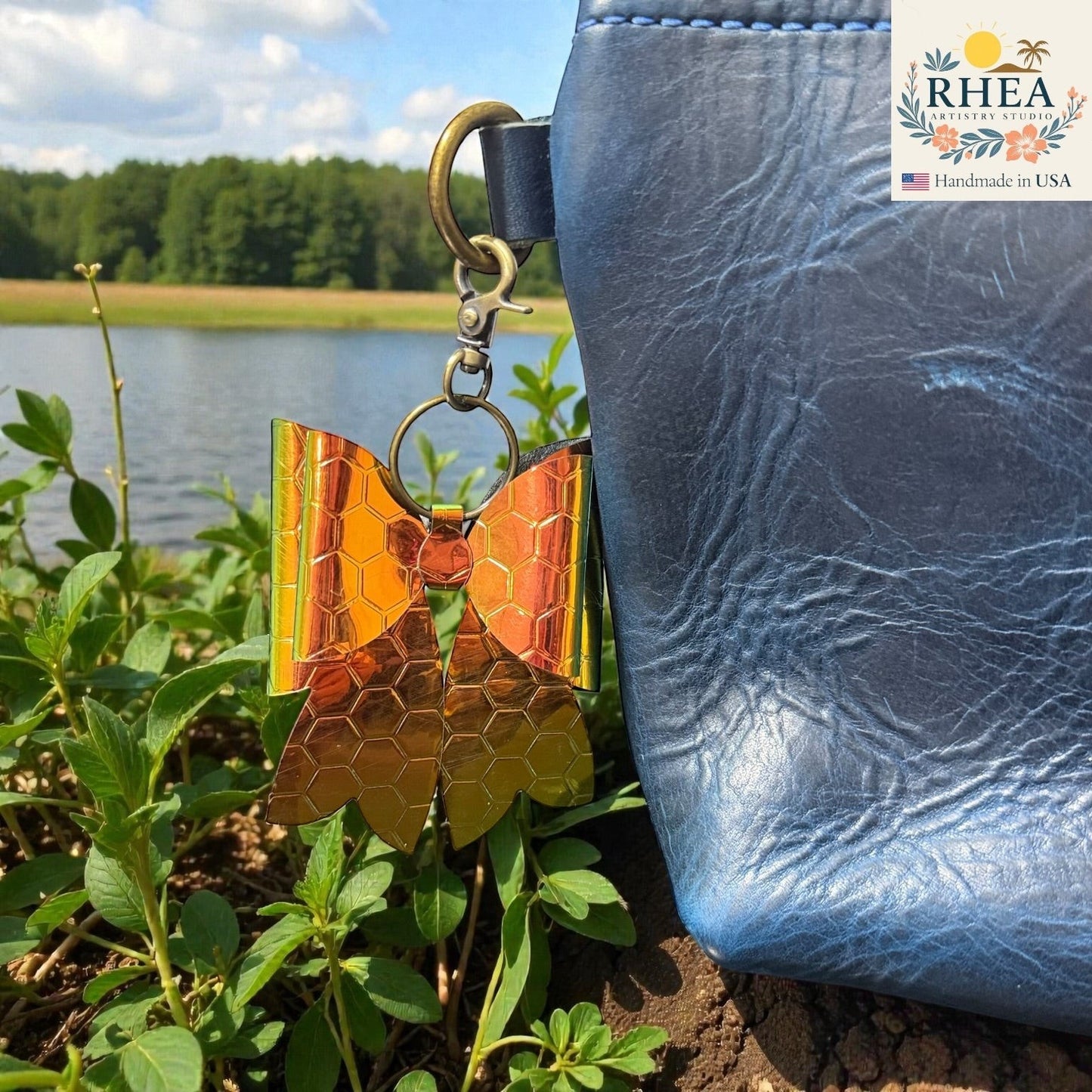 Rhea Artistry Studio holographic bow bag charm with honeycomb pattern and brass hardware, attached to a blue leather bag.