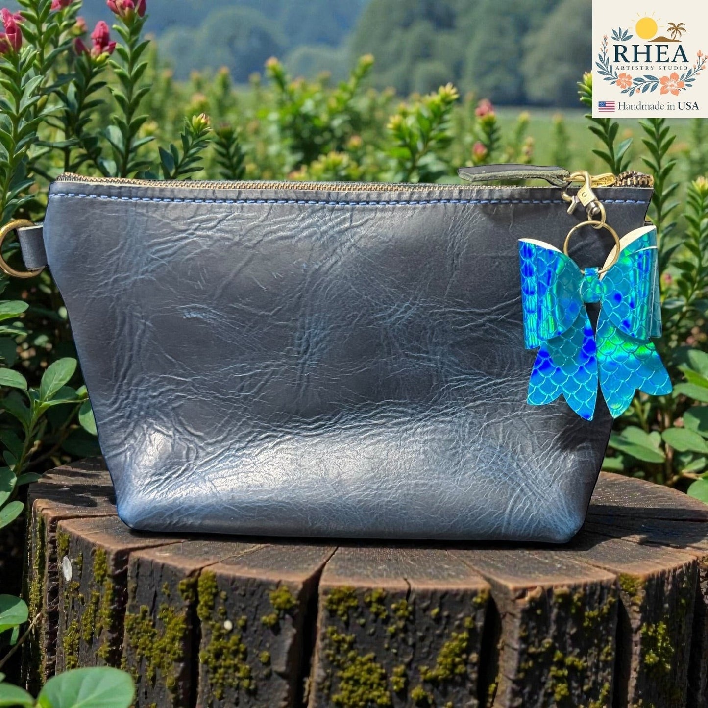 Rhea Artistry Studio holographic blue mermaid scale bow bag charm with brass hardware, attached to a grey faux leather pouch.
