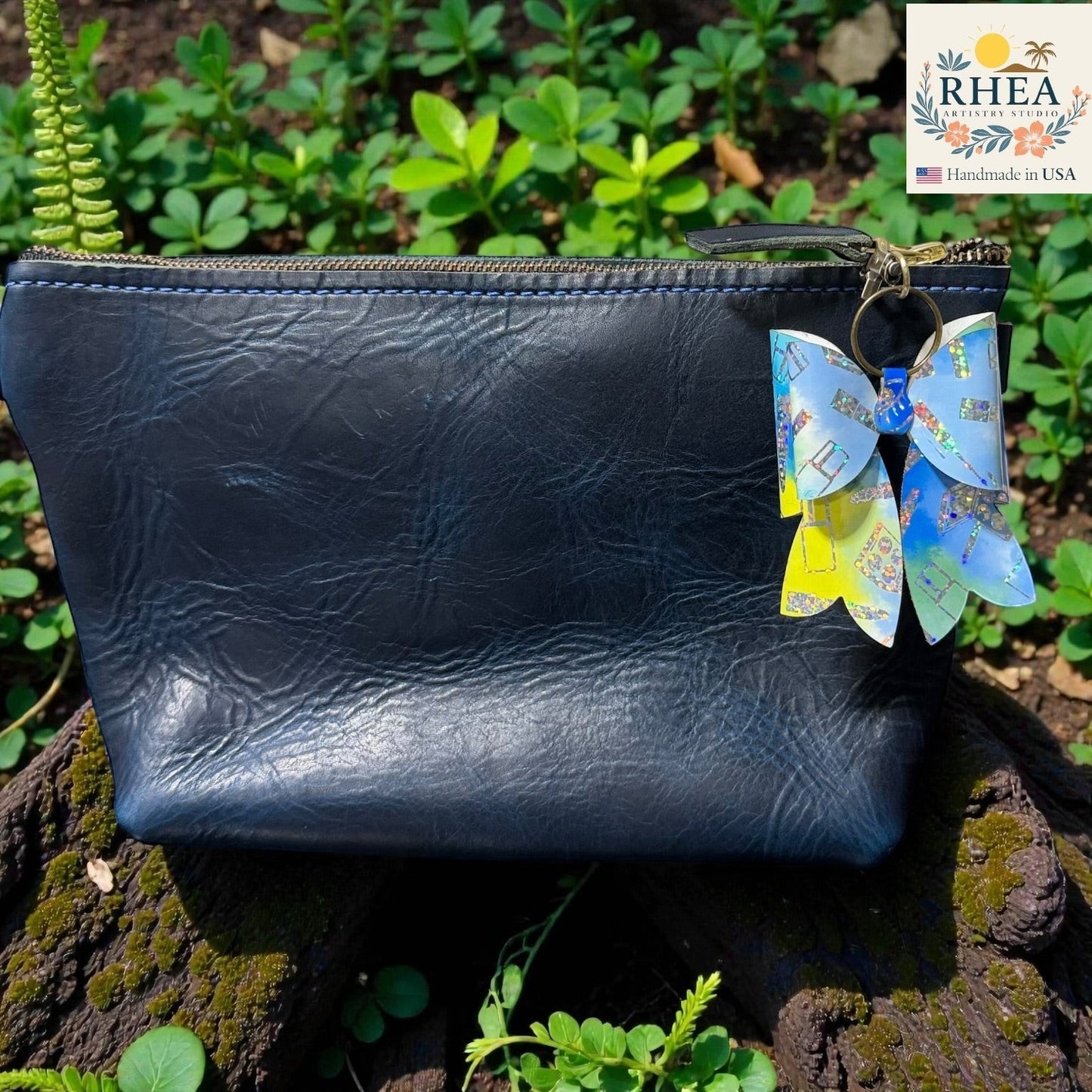 Rhea Artistry Studio holographic double-layer French bow bag charm with blue and yellow accents, attached to a navy blue leather pouch.