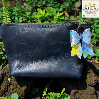 Rhea Artistry Studio holographic double-layer French bow bag charm with blue and yellow accents, attached to a navy blue leather pouch.