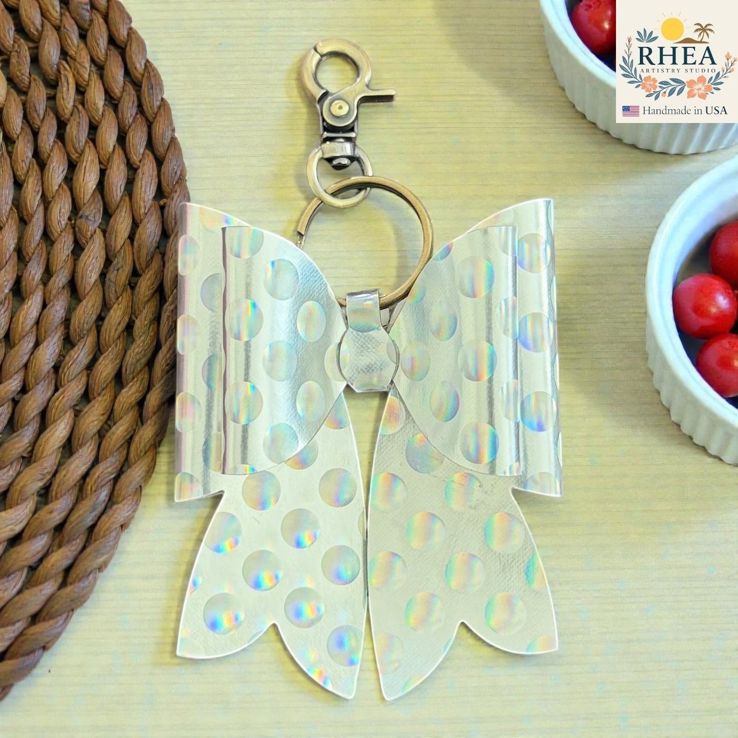 Rhea Artistry Studio holographic silver bow bag charm with white polka dots and brass hardware.