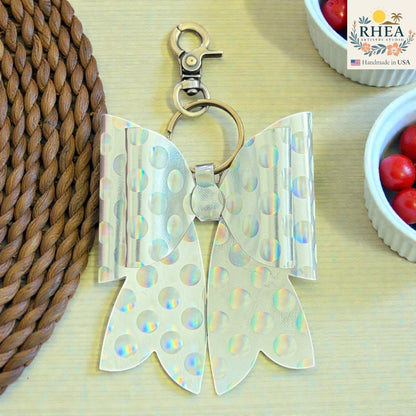 Rhea Artistry Studio holographic silver bow bag charm with white polka dots and brass hardware.