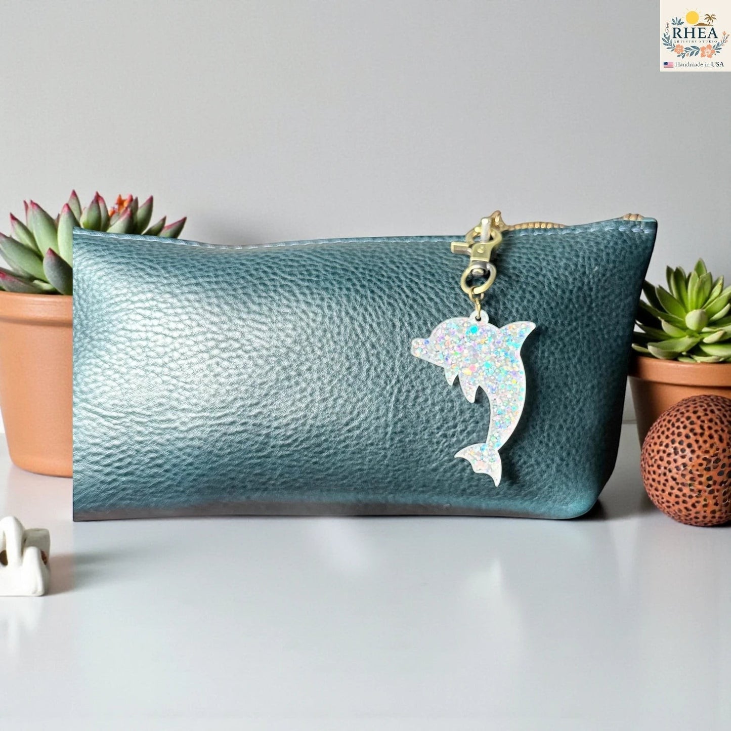 Rhea Artistry Studio holographic dolphin acrylic charm with brass clasp on a teal bag.
