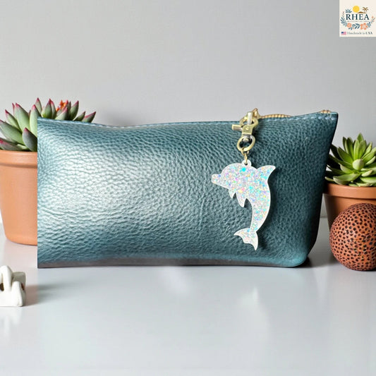 Rhea Artistry Studio holographic dolphin acrylic charm with brass clasp on a teal bag.
