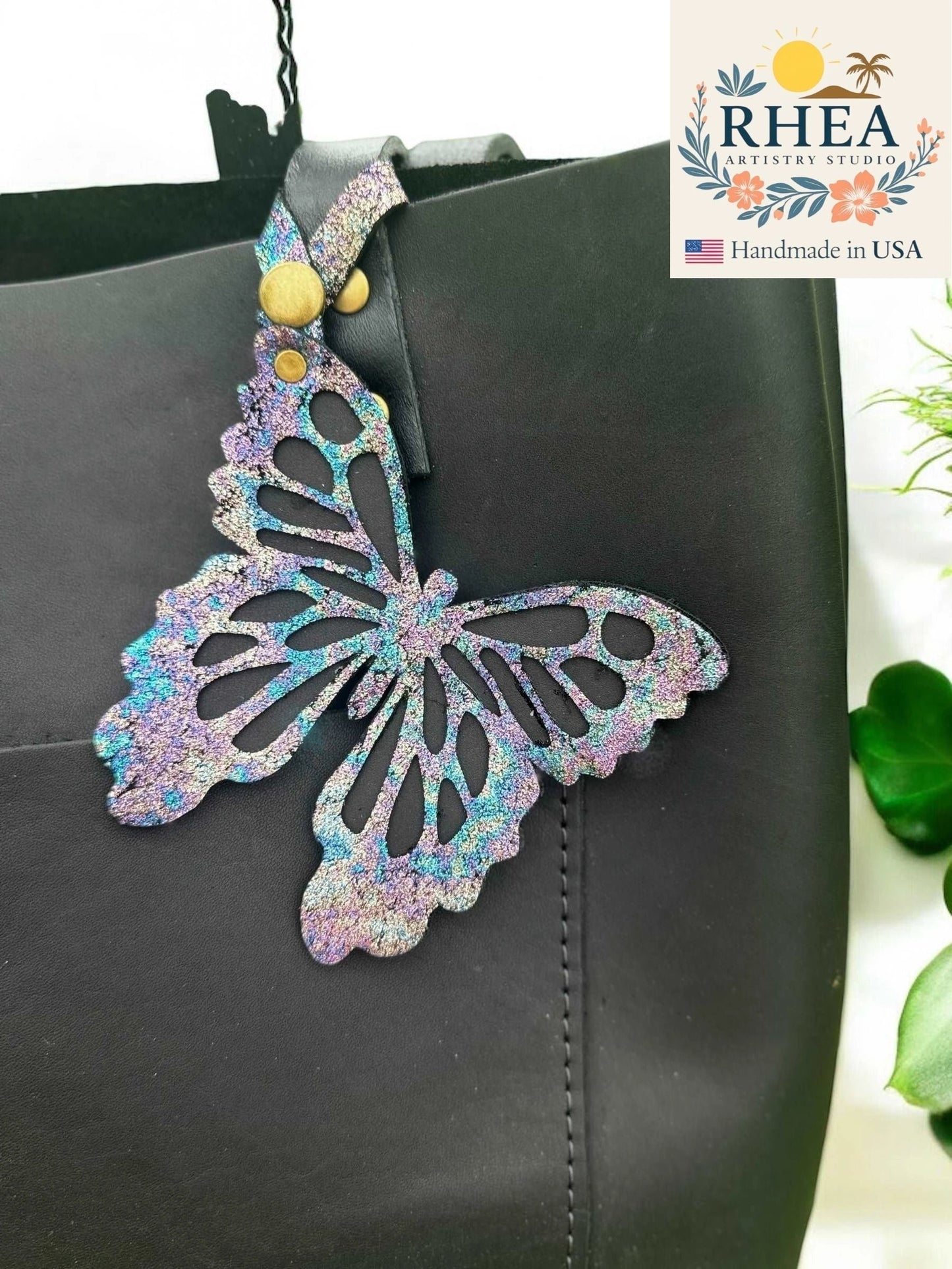 Rhea Artistry Studio iridescent leather butterfly charm with metallic finish attached to a black tote bag.