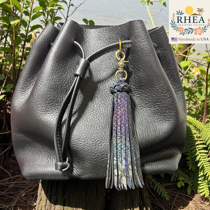 Rhea Artistry Studio handmade black leather bag charm with a long, dual-tone iridescent tassel and antique brass lobster clasp.