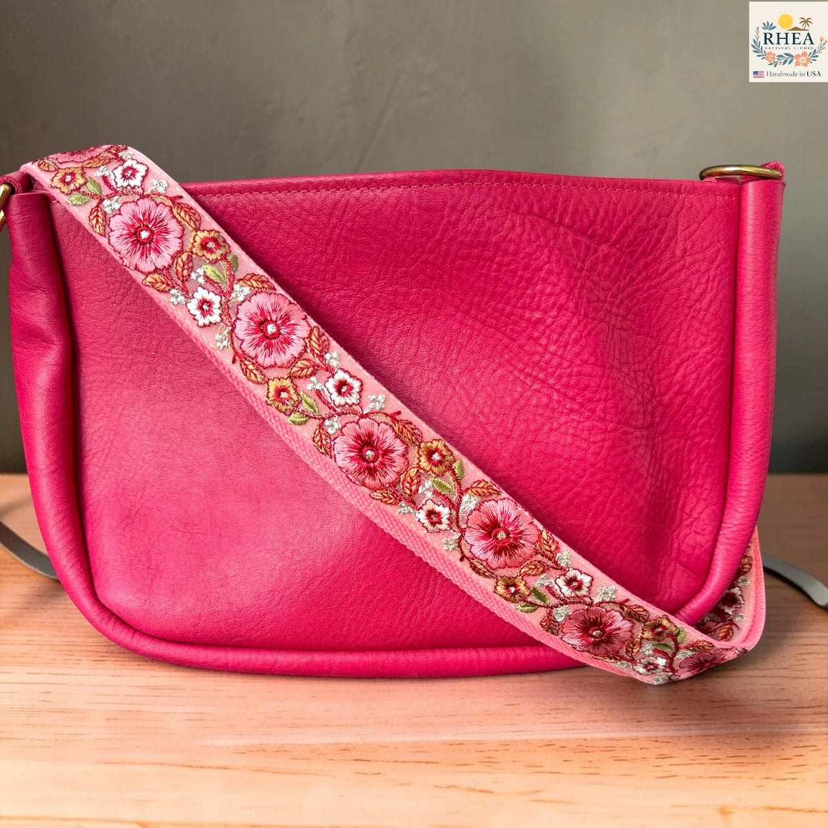 Rhea Artistry Studio ivory crossbody strap with coral and red floral embroidery with green leaf accents, 1.5-inch width, adjustable length.
