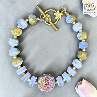 Rhea Artistry Studio handmade bracelet with lavender and gold glass beads, floral focal bead, and brass toggle clasp with star detail.