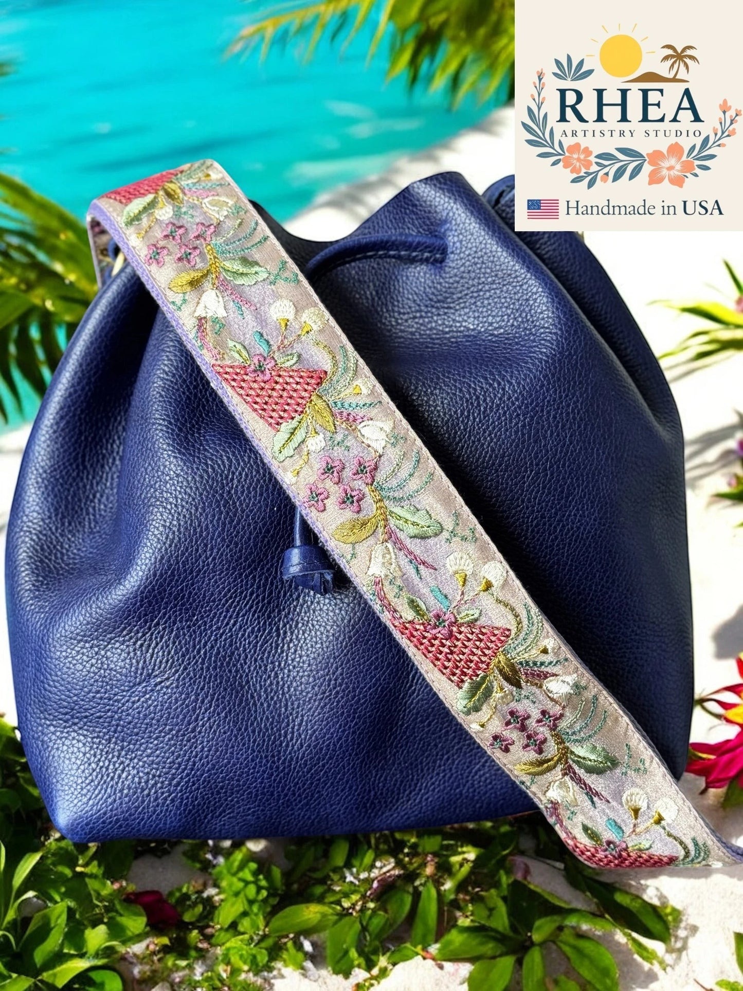Rhea Artistry Studio lavender and purple embroidered crossbody strap with floral and basket motifs on a navy blue leather bag.