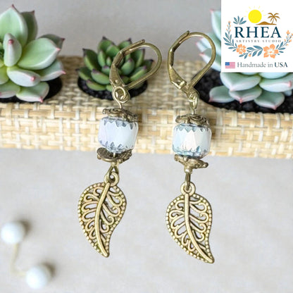 Rhea Artistry Studio antique brass leaf drop earrings with white faceted glass beads and Bali-style spacers, 2 inches long.