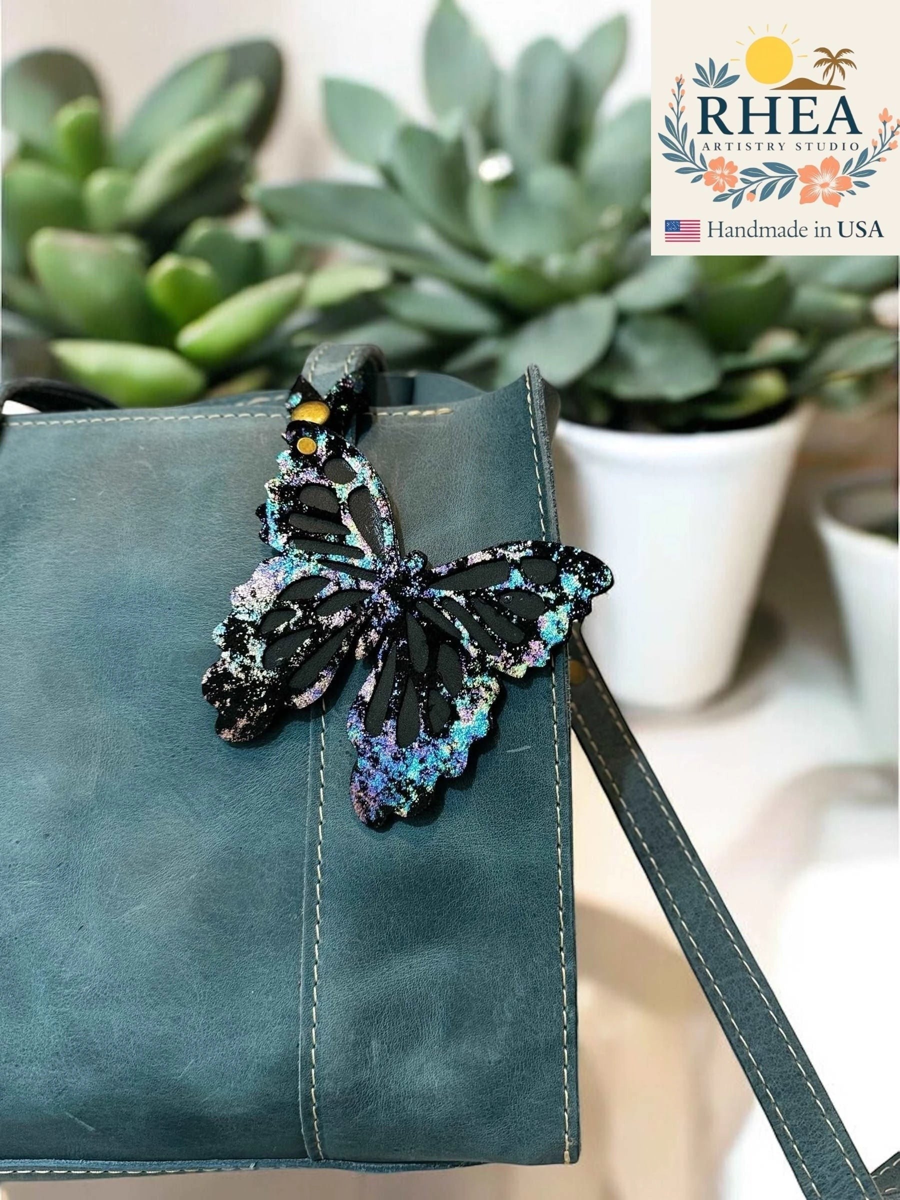 Rhea Artistry Studio black leather butterfly charm with iridescent and metallic finish, attached to a teal purse.