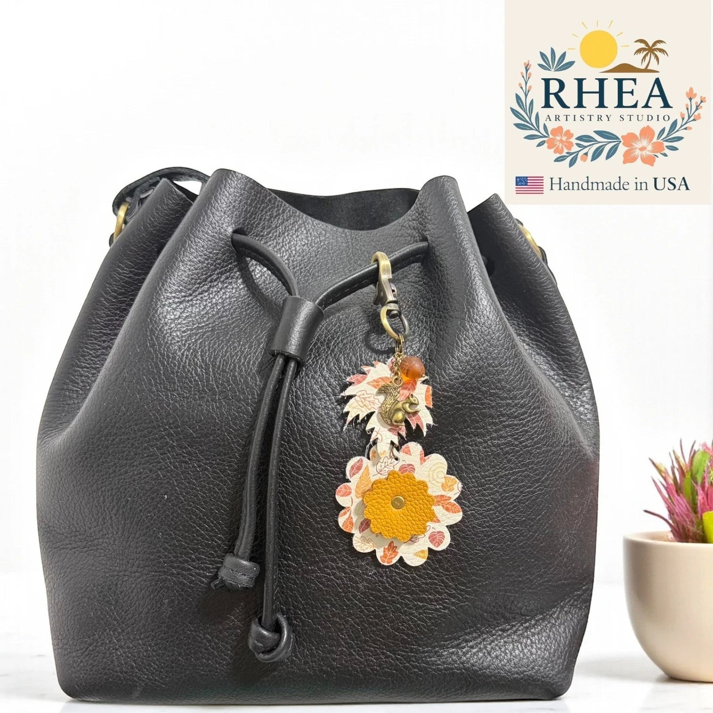 Rhea Artistry Studio black leather drawstring bag with acorn and squirrel charms featuring fall leaf patterns and a yellow flower.