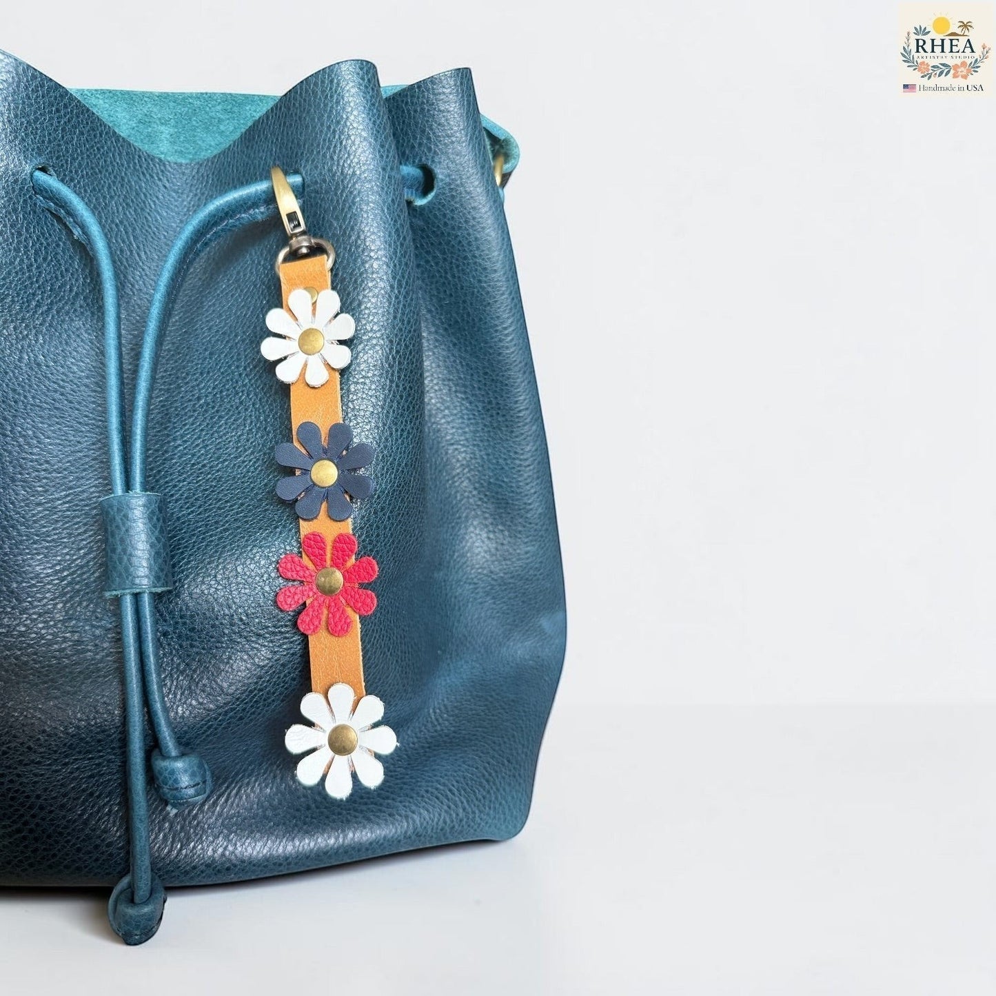 Rhea Artistry Studio handmade leather daisy bag charm with white, red and blue flowers and brass rivets.