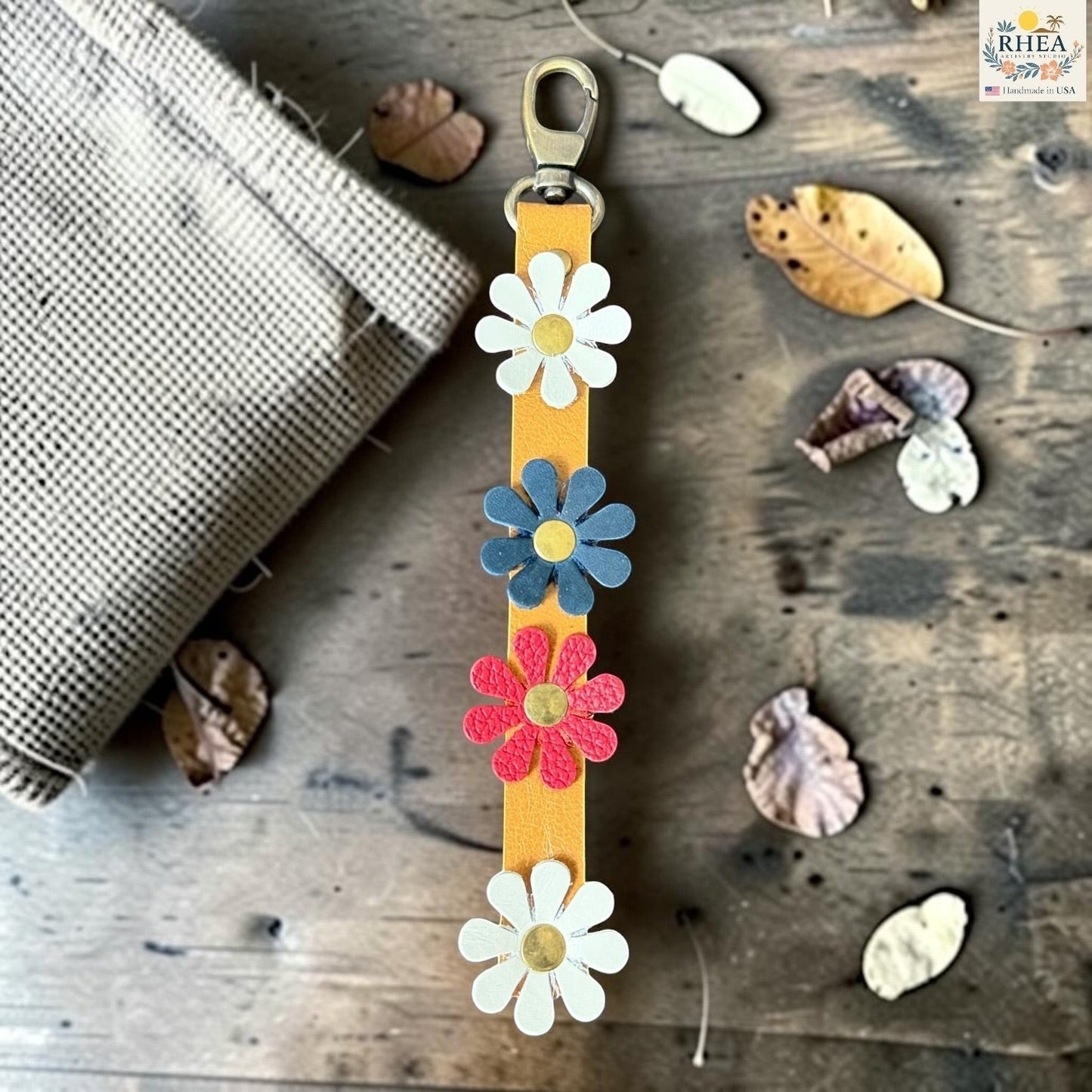 Rhea Artistry Studio handmade leather daisy bag charm with white, red and blue flowers and brass rivets.