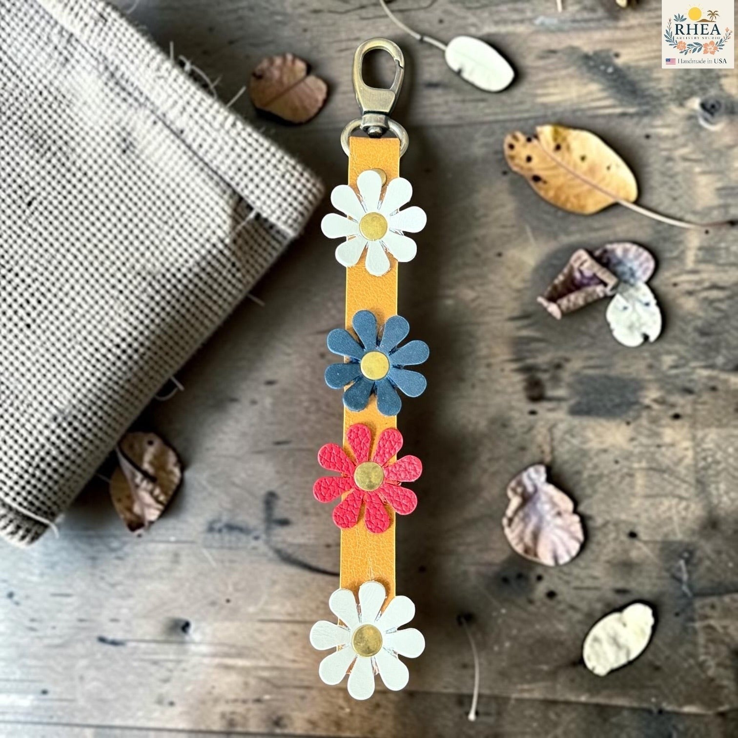 Rhea Artistry Studio handmade leather daisy bag charm with white, red and blue flowers and brass rivets.