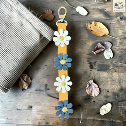 Rhea Artistry Studio handmade leather daisy bag charm with white and blue flowers and brass rivets.