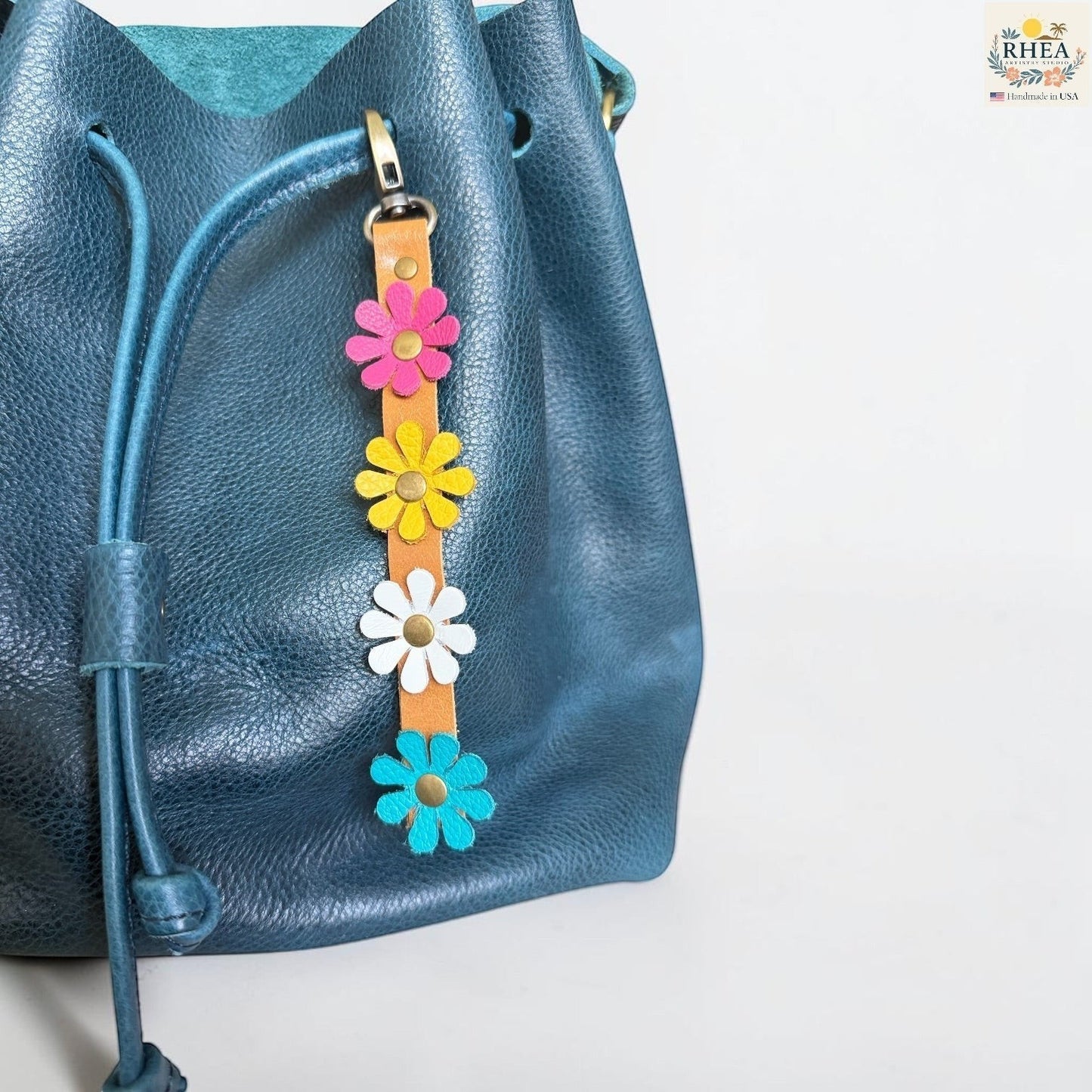 Rhea Artistry Studio handmade leather daisy wristlet keychain with pink, yellow, and blue flowers attached to a tan leather strap with brass rivets.