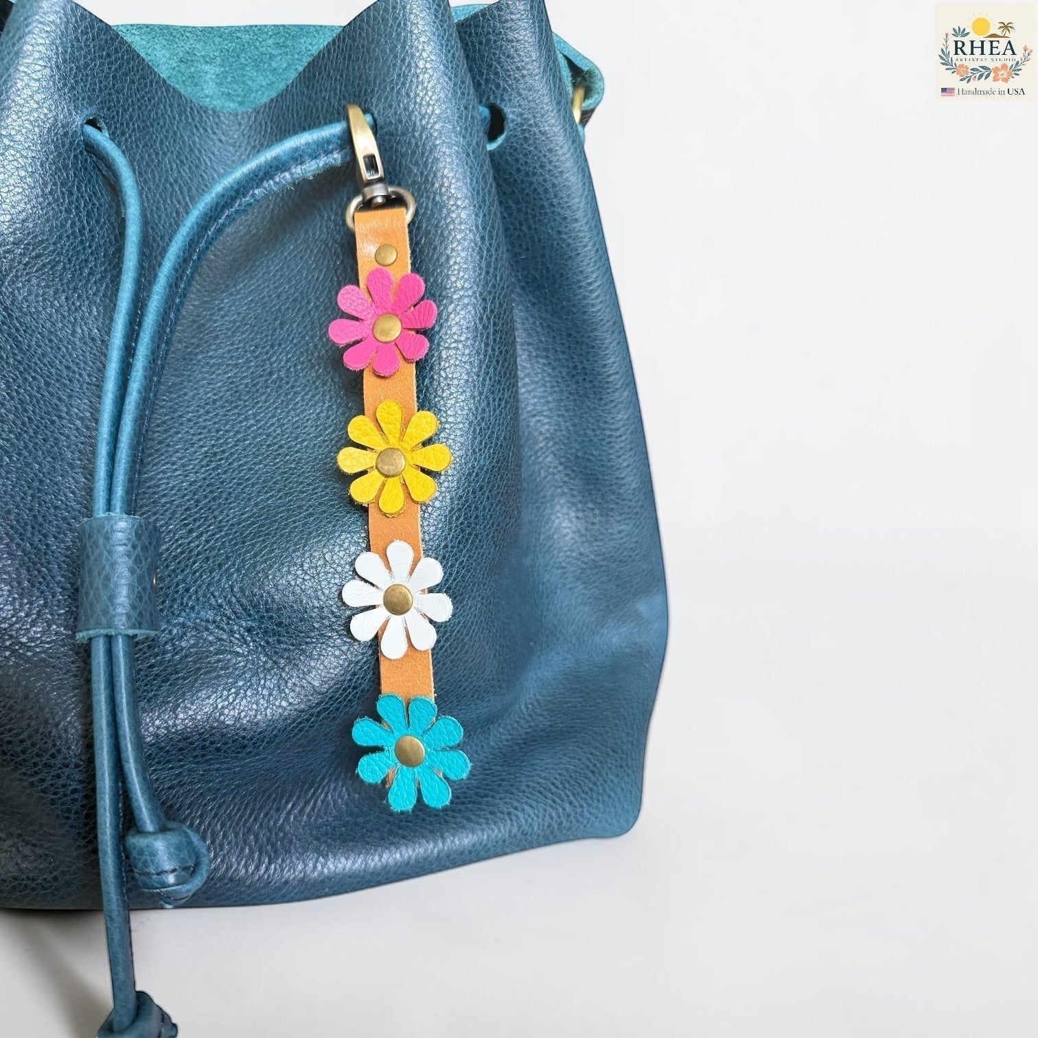 Rhea Artistry Studio handmade leather daisy wristlet keychain with pink, yellow, and blue flowers attached to a tan leather strap with brass rivets.