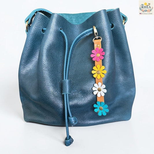 Rhea Artistry Studio handmade leather daisy bag charm with pink, yellow, white, and teal flowers and brass rivets.