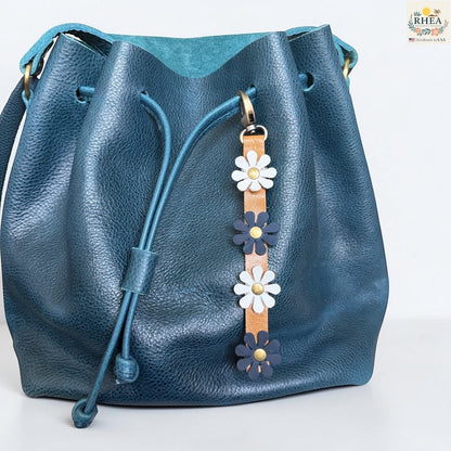 Rhea Artistry Studio handmade leather daisy bag charm with white and blue flowers and brass rivets.