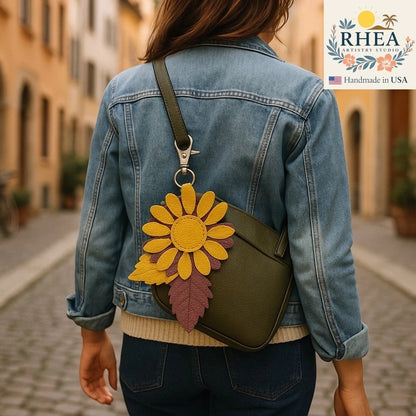 Rhea Artistry Studio yellow and purple leather daisy charm with leaf detail attached to a green crossbody bag.