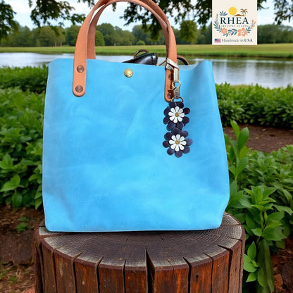 Rhea Artistry Studio handmade double-layer leather daisy charm in navy and white, attached to a bright blue tote bag.