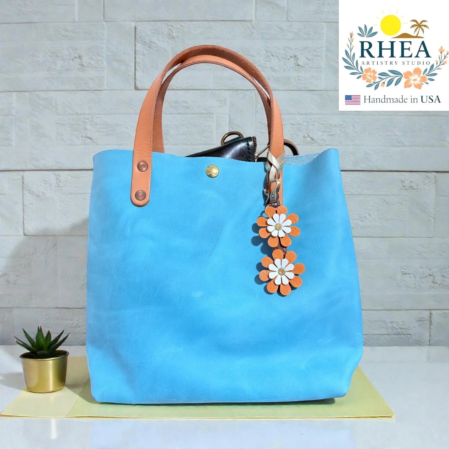 Rhea Artistry Studio double-layer leather daisy purse charm in orange and white, attached to a blue tote bag.